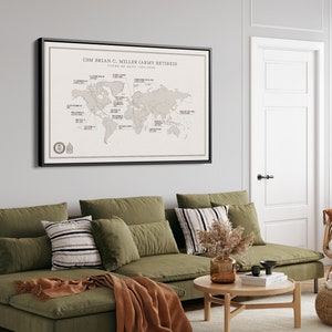 May include: A framed world map with pins marking locations around the globe. The map is titled "CSM Brian C. Miller (Army Retired) Tours of Duty 1993-2022". The map is hanging on a wall in a living room with a green sectional sofa and a wooden coffee table.