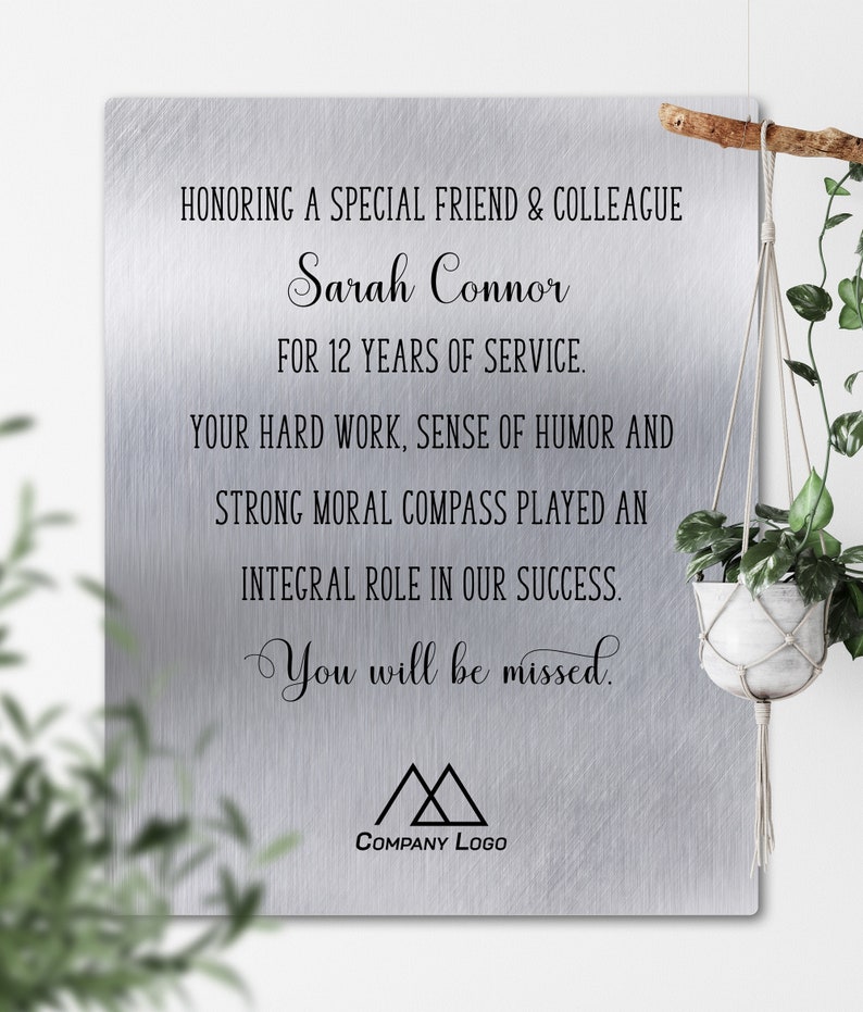 May include: A silver plaque with a brushed metal finish honoring Sarah Connor for 12 years of service. The plaque reads "Honoring a special friend & colleague Sarah Connor for 12 years of service. Your hard work, sense of humor and strong moral compass played an integral role in our success. You will be missed." The plaque also features a company logo with two triangles.
