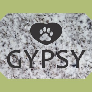 May include: A white granite pet memorial with a black heart and paw print design. The name "GYPSY" is written in black lettering.