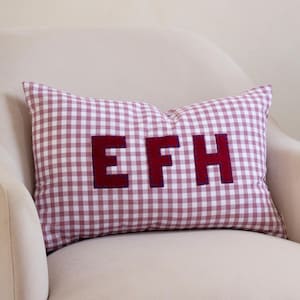 May include: A rectangular throw pillow featuring a pink and white gingham check pattern. The centre of the pillow displays the letters E, F, and H in a dark maroon fabric, each individually stitched onto the surface with blue thread.