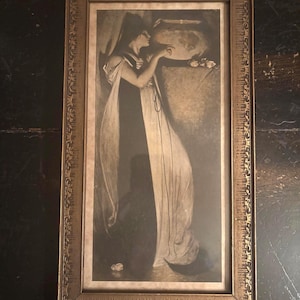 May include: An antique framed print featuring a woman in a flowing gown. The sepia-toned artwork depicts a classical scene with a woman draped in fabric, set against a dark background. The frame is ornate with a gold finish.