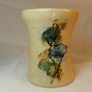 May include: A cream-colored ceramic vase with a speckled glaze and a hand-painted design of blue and green flowers.