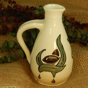 May include: White ceramic pitcher with a green and brown leaf design. The pitcher has a handle and a rounded body.
