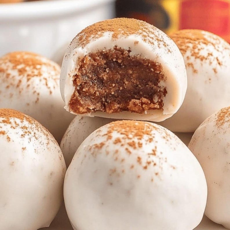 Puede incluir: Primer plano de varias trufas recubiertas de blanco, algunas espolvoreadas con canela. Una trufa est&aacute; cortada, revelando un interior marr&oacute;n oscuro. Las trufas est&aacute;n apiladas, sugiriendo un postre o confiter&iacute;a.
