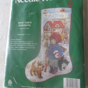 May include: A needlepoint kit for a Christmas stocking featuring a winter scene with a child, two dogs, and a house. The stocking is titled "Tiny Tim's Stocking" and the house has the name "Timothy" above the door. The kit includes 100% wool yarn, felt backing, and complete instructions.