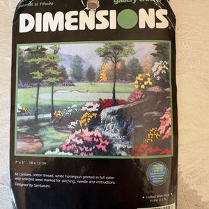 May include: A Dimensions gallery crewel kit featuring a landscape scene with a waterfall, trees, and colorful flowers. The kit measures 7" x 5" and includes cotton thread, needle, and instructions. The package has the text "Waterfall at Fifteen".