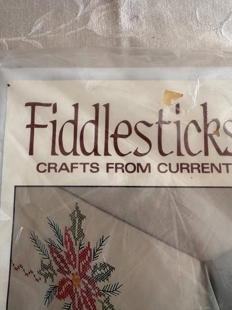 K&ouml;nnte beinhalten: Ein Bastelset mit dem Text "Fiddlesticks CRAFTS FROM CURRENT". Das Set zeigt ein Kreuzstichdesign einer roten und gr&uuml;nen Weihnachtssternblume. Das Set befindet sich in einer transparenten Kunststoffverpackung.