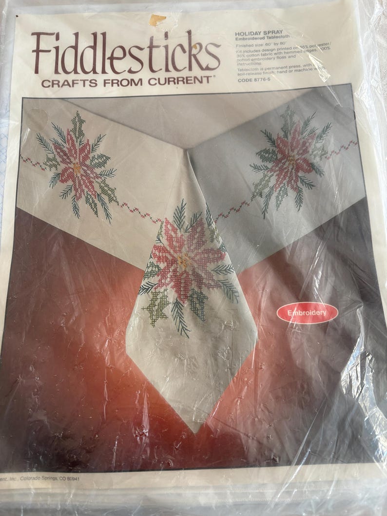 K&ouml;nnte beinhalten: Ein Fiddlesticks Stickset f&uuml;r eine Weihnachtstischdecke. Das Design zeigt ein Kreuzstichmuster aus Weihnachtsstern und Gr&uuml;n in Rot und Gr&uuml;n auf einem cremefarbenen Stoff. Die Verpackung ist in Kunststoff versiegelt. Fertige Gr&ouml;&szlig;e: 152 x 203 cm.