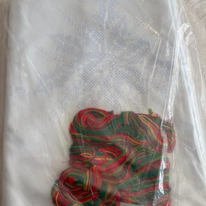 K&ouml;nnte beinhalten: Ein wei&szlig;er Stoff mit blauem Schneeflockenmuster, verpackt in durchsichtigem Kunststoff.  Mit rotem, gr&uuml;nem und gelbem Stickgarn. Ein Bastelset f&uuml;r Nadelmalerei oder Kreuzstich.