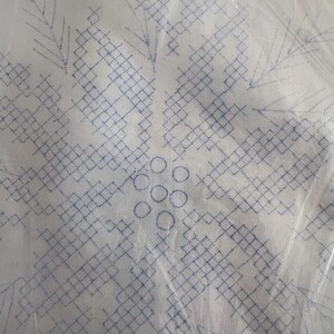 K&ouml;nnte beinhalten: Wei&szlig;er Stoff mit einem blau gestickten Schneeflockenmuster. Die Schneeflocke besteht aus geometrischen Formen und Kreisen mit einem detaillierten, symmetrischen Muster. Der Stoff ist in klarem Kunststoff verpackt.