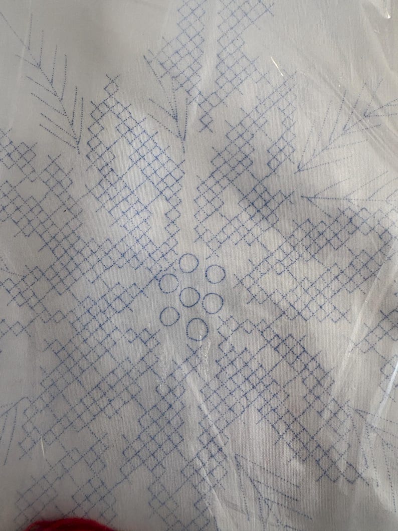 K&ouml;nnte beinhalten: Wei&szlig;er Stoff mit einem blau gestickten Schneeflockenmuster. Die Schneeflocke besteht aus geometrischen Formen und Kreisen mit einem detaillierten, symmetrischen Muster. Der Stoff ist in klarem Kunststoff verpackt.