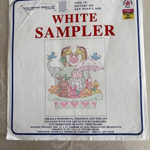 May include: A white sampler kit featuring a cross-stitch design of Noah's Ark with animals, hearts, and an umbrella. The text "WHITE SAMPLER" is prominently displayed. The kit includes a 12" x 15" sampler of poly/cotton broadcloth.