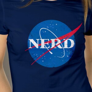 May include: A navy blue t-shirt with a distressed blue and red NASA logo that says "NERD" in white letters.