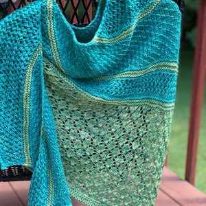 May include: A teal and green knitted shawl with a lacy pattern. The shawl is draped over a wicker chair.