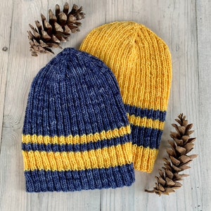 Puede incluir: Dos gorros de punto con rayas amarillas y azules. El gorro de la izquierda es azul con rayas amarillas, y el gorro de la derecha es amarillo con rayas azules.