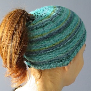 Könnte beinhalten: Eine gestrickte Mütze in den Farben Türkis, Grün und Blau mit einem Loch für einen Pferdeschwanz hinten.