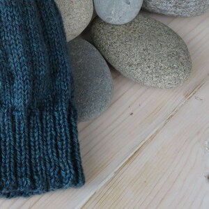 Puede incluir: Un gorro de punto azul turquesa con borde de canal&eacute;, apoyado sobre una superficie de madera clara.