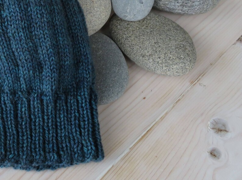 Puede incluir: Un gorro de punto azul turquesa con borde de canal&eacute;, apoyado sobre una superficie de madera clara.