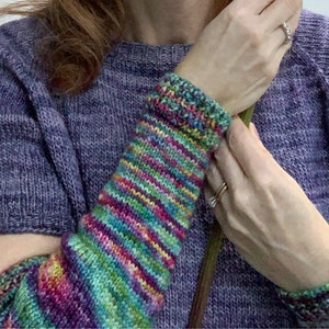Puede incluir: Un par de calentadores de brazo de punto de rayas de colores. Los calentadores de brazo están hechos con una variedad de colores, incluyendo rosa, morado, verde, azul y amarillo. Los calentadores de brazo se usan en los brazos de una persona.