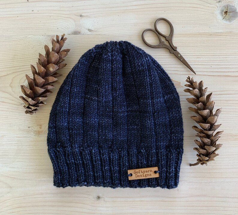 Puede incluir: Un gorro de punto azul oscuro con una etiqueta de cuero marr&oacute;n que dice "Soft yarn Designs".
