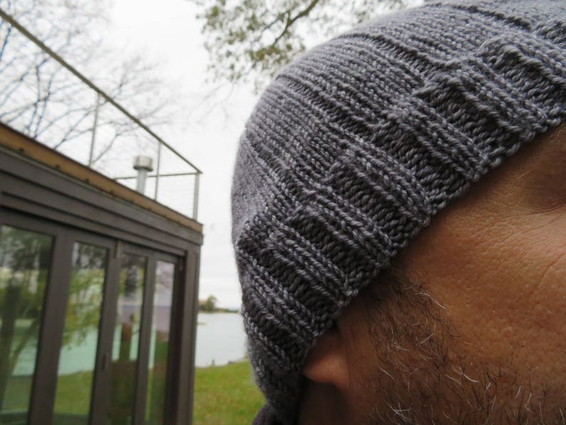 Puede incluir: Primer plano de un gorro de punto gris. El gorro est&aacute; hecho de un hilo suave y texturizado y tiene un dise&ntilde;o simple y cl&aacute;sico.