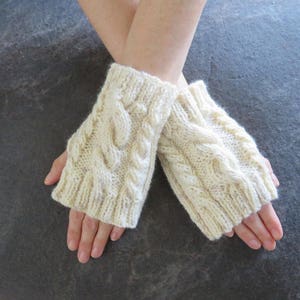 Könnte beinhalten: Ein Paar weiße gestrickte Fingerhandschuhe mit einem Zopfmuster.