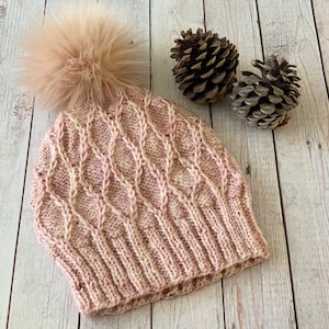 May include: A pink knitted hat with a white cable knit pattern and a fluffy pom pom on top.