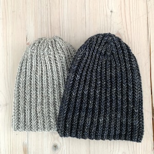 Pode incluir: Dois gorros de malha canelada. Um é cinza claro e o outro azul marinho escuro. Os gorros são feitos de um fio macio e texturizado e têm um design clássico e simples. Os chapéus são provavelmente feitos à mão e adequados para o clima frio.