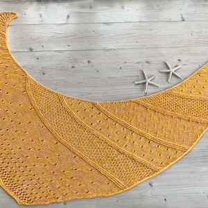 May include: A yellow knitted shawl with a lacy pattern. The shawl is draped over a wooden surface.