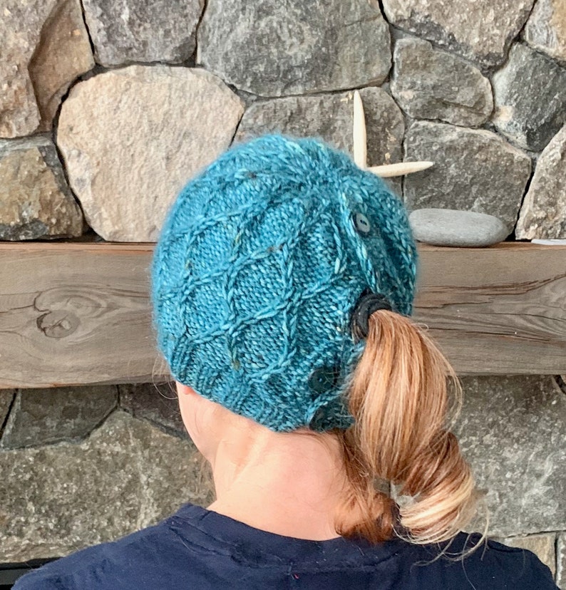 A woman is seen from behind wearing a knitted hat with buttons, allowing her ponytail to stick out.