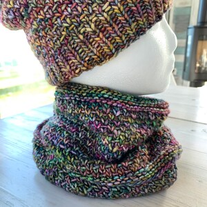 May include: A colorful knitted hat and matching neck warmer. The hat is a slouchy beanie style with a multi-colored yarn. The neck warmer is a cowl style with a similar yarn.