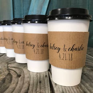 May include: Set of six white coffee cups with brown paper sleeves. The sleeves have the text "kelsey & charlie 4.21.18" printed on them.