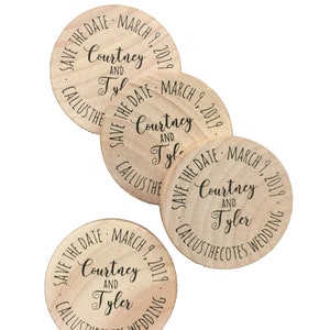 May include: A collection of wooden wedding favors. Each circular favor has the text "SAVE THE DATE MARCH 9, 2019" and the names "Courtney and Tyler" printed in black. The favors are made of light-colored wood.