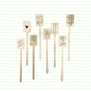 May include: Set of eight wooden stick drink stirrers with various sayings and designs. The sayings include "Happy Birthday", "Congrats! You Did It!", "Bless Your Heart", "Happy Anniversary", "Mr. & Mrs.", "Drink Up", and two with hearts.