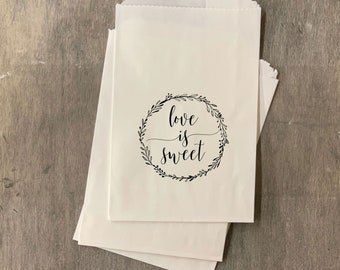 May include: White paper favor bags with a black floral wreath and the text "love is sweet" printed on the front.