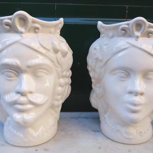 Könnte beinhalten: Zwei weiße Keramikvasen in Form von menschlichen Köpfen. Die Vasen haben aufwendige Details und sind ein traditionelles italienisches Design.