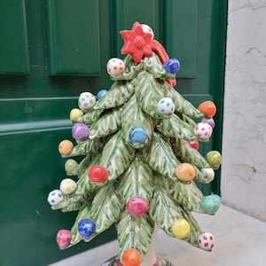 Könnte beinhalten: Ein Keramik-Weihnachtsbaum-Anhänger mit grüner Basis und bunten, gepunkteten Ornamenten. Der Baum ist mit einem roten Stern oben verziert.