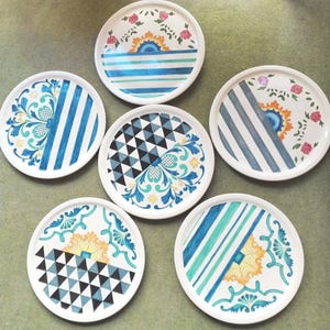 Puede incluir: Seis platos de cerámica decorativos con varios patrones geométricos azules, verdes, amarillos y blancos. Los platos tienen un fondo blanco y presentan una variedad de diseños, que incluyen rayas, triángulos y motivos florales.