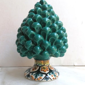 Puede incluir: Una escultura de cerámica en forma de piña con un acabado esmaltado verde y una base colorida y estampada.