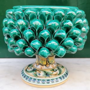 Puede incluir: Un cuenco de cerámica verde con forma de piña con una base detallada y colorida. El cuenco está hecho en un estilo tradicional y tiene un acabado brillante.