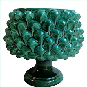 May include: A green ceramic planter shaped like a pine cone with a wide base. The planter has a glossy finish and is perfect for displaying plants or flowers.