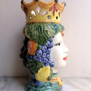 Peut inclure: Un vase en céramique en forme de tête de femme avec une couronne sur le dessus. Le vase est décoré de fruits et de fleurs dans des tons de vert, bleu, jaune et rouge.