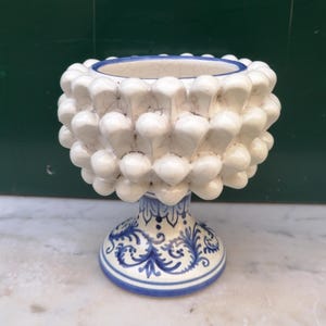 Puede incluir: Un cuenco de cerámica blanca con forma de piña con una base de patrón azul y blanco. El cuenco es una pieza decorativa y es perfecto para guardar objetos pequeños.