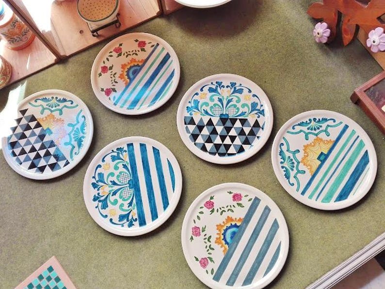May include: Set of six decorative ceramic plates with various colorful patterns. The plates feature geometric designs, floral motifs, and stripes in shades of blue, green, yellow, and white.