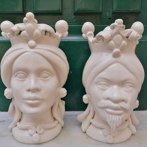 Könnte beinhalten: Zwei weiße Keramikskulpturen von Gesichtern, eine mit einer Krone und die andere mit einem Turban. Beide Skulpturen haben detaillierte Gesichtszüge und sind in einem traditionellen Stil gehalten.