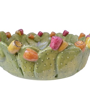 Puede incluir: Un cuenco de cerámica verde con forma de cactus con flores de colores. El cuenco es perfecto para servir aperitivos o guardar objetos pequeños.