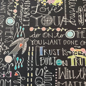 May include: Black fabric with white handwritten text, including phrases like "Love You" and "Trust is Built." The design features floral and button accents in pink, green, and teal. A decorative and inspirational design.