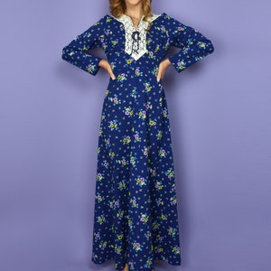 Puede incluir: Un vestido largo azul maxi con cuello de encaje blanco y estampado floral. El vestido tiene mangas largas y un lazo en el cuello.