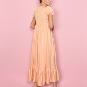 May include: A peach-colored maxi dress with a ruffled hem and short puff sleeves. The dress has a fitted bodice and a flowy skirt.