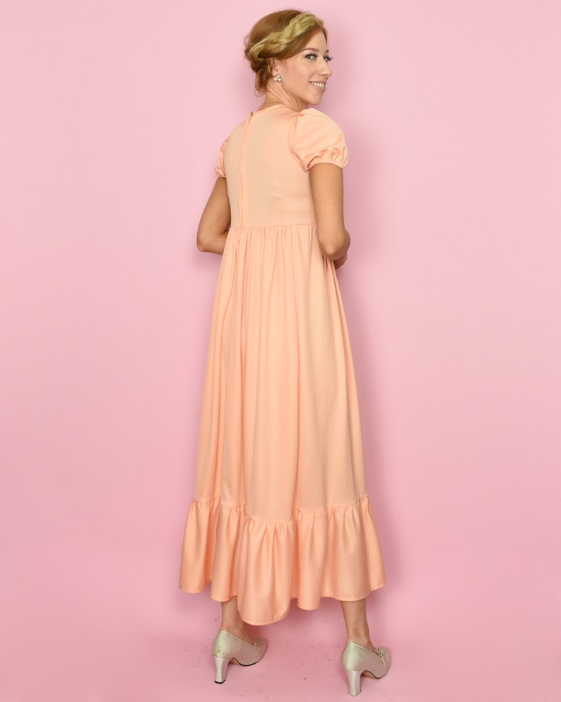 May include: A peach-colored maxi dress with a ruffled hem and short puff sleeves. The dress has a fitted bodice and a flowy skirt.